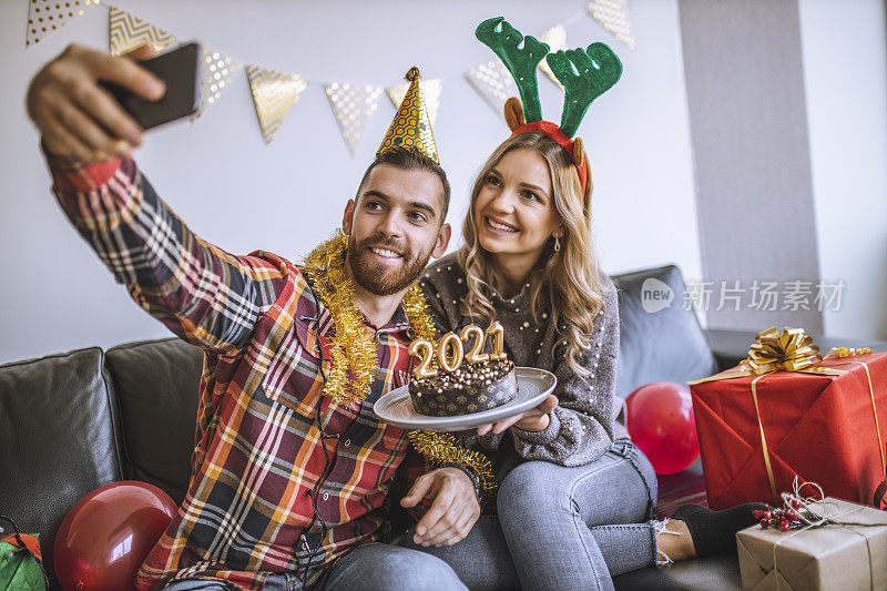 一对夫妇在家庆祝圣诞节，他们拿着巧克力蛋糕，蛋糕上点燃了2021年的数字蜡烛，并和朋友们进行视频通话
