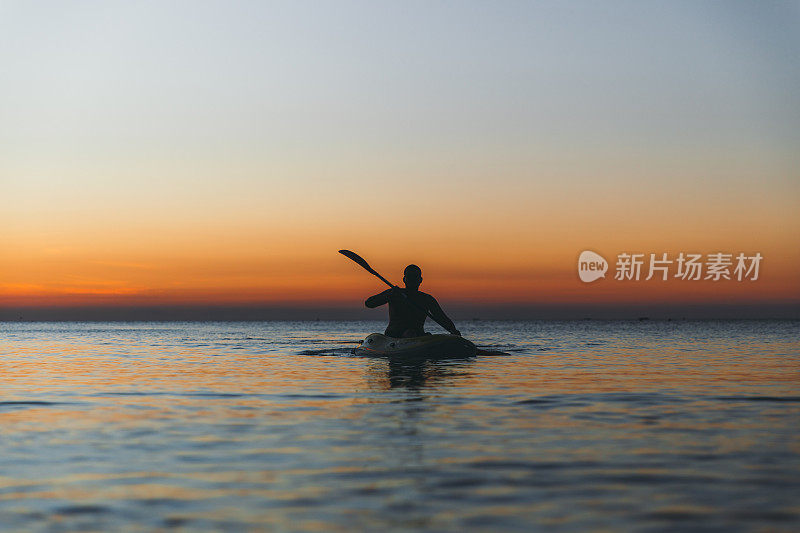 在桑给巴尔岛美丽的日落中，一个年轻人在海洋中划着皮艇