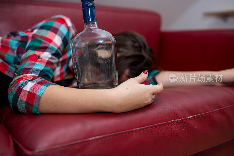一个喝醉了的女人躺在沙发上，手里拿着一个空瓶子