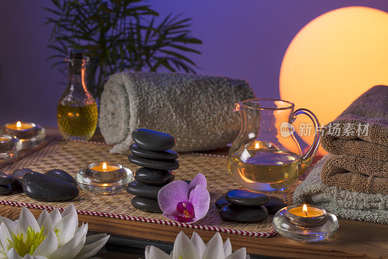 美容spa概念-黑色按摩石，兰花花，蜡烛，毛巾和按摩油在木桌子上浮动睡莲