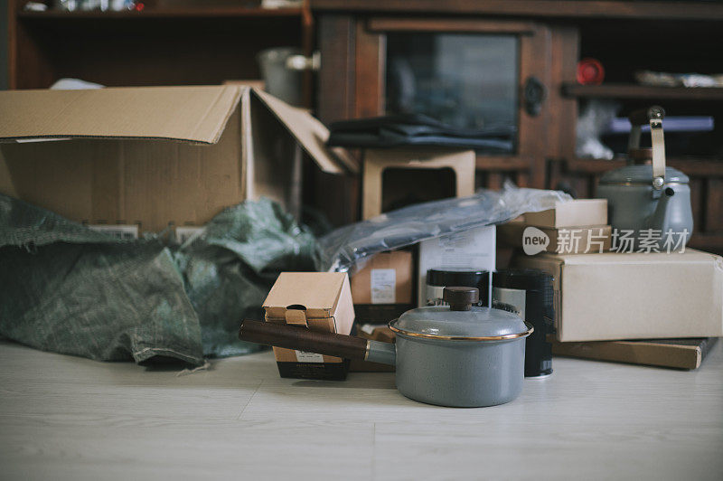 打开的纸板箱，客厅地板上有网上购物壶和平底锅
