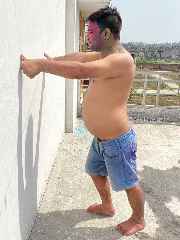 赤裸上身，裹着漆粉的印度男子冲在白色墙壁上，在胡里节的色彩和爱漆大战中胡闹，面带微笑
