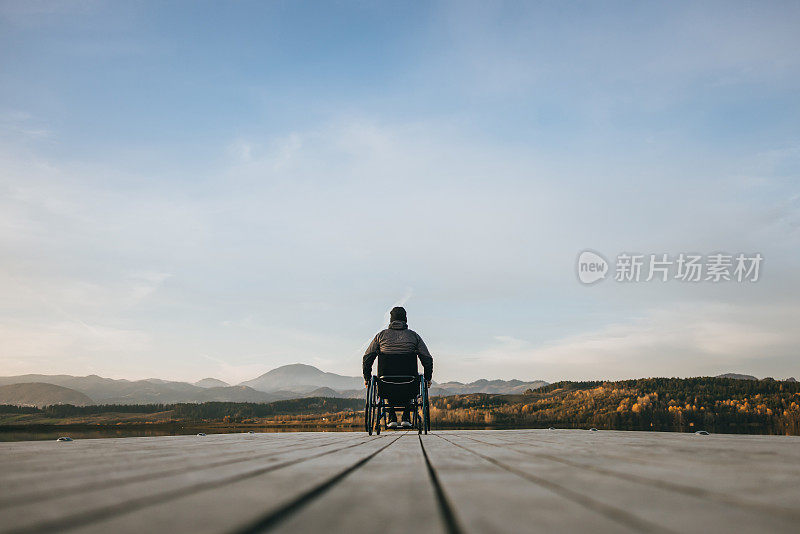 一名残疾人坐在轮椅上，在湖滨码头边欣赏风景