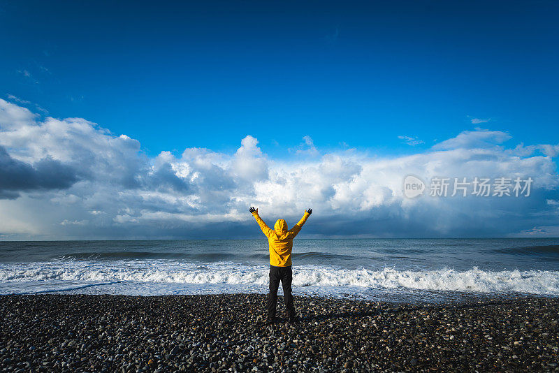 一名男子在海边穿着黄色夹克，举起双臂