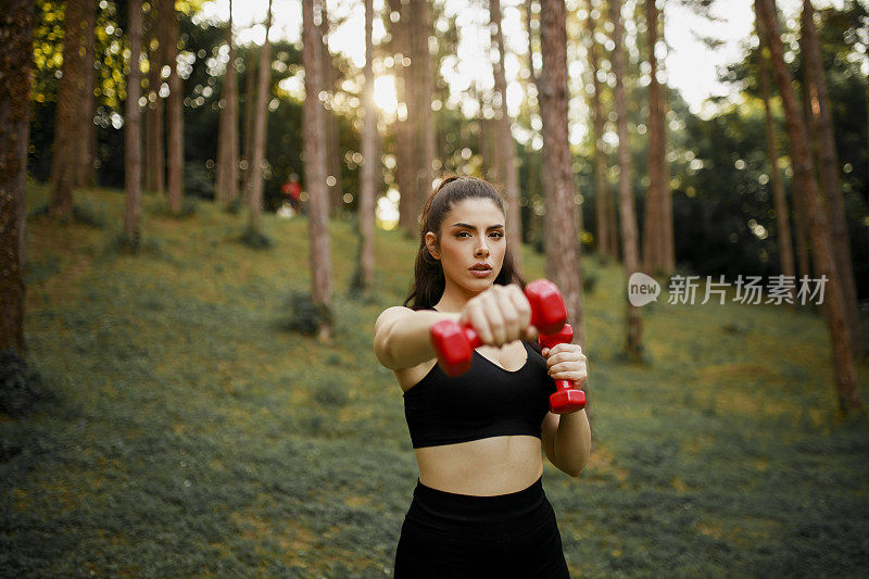 一个漂亮的女人在锻炼的时候用了哑铃。女人伸展和锻炼与重量户外