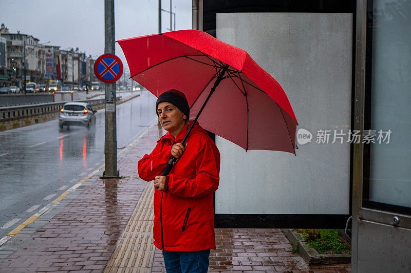 一位女士在雨天撑着伞在公共交通车站等车