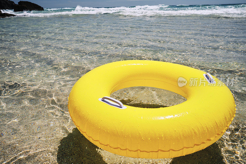 6月的一个阳光明媚的日子，黄色的橡胶环漂浮在康沃尔郡佩德旺德海滩浅浅的清澈的蓝色大海上。