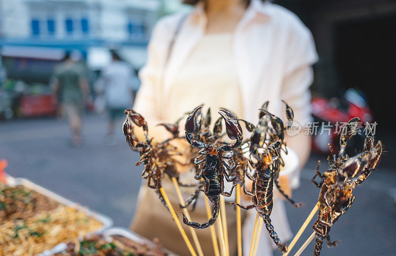 在泰国曼谷当地的街头小食市场，亚洲当地的年轻人戴着口罩在耀华购买火虫