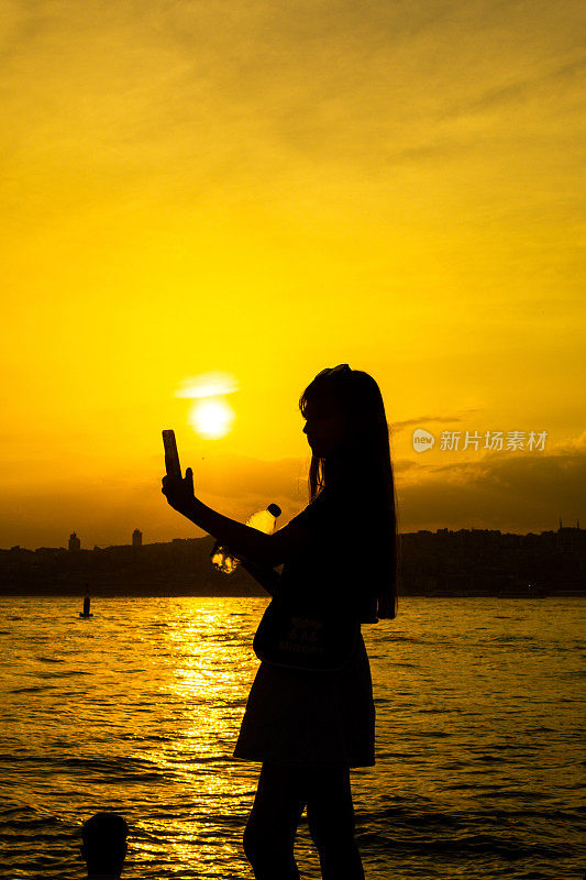 日落时使用手机的美丽女孩的剪影