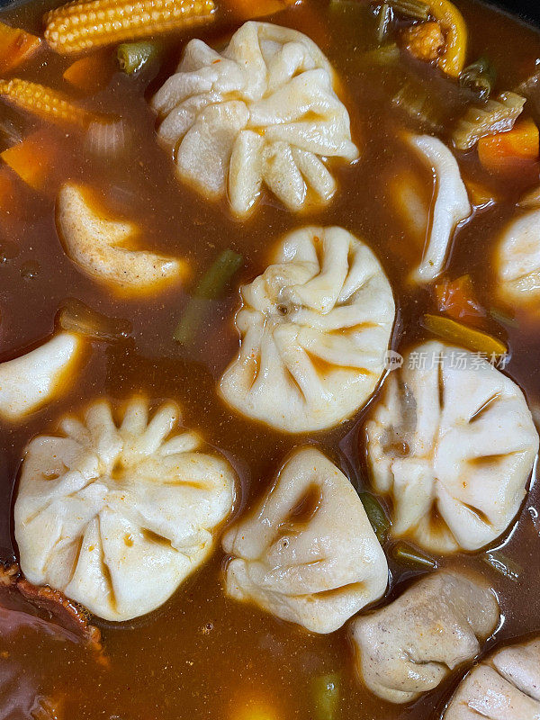 一碗Momos(南亚饺子)的全框图像，白面粉和水面团填充鸡肉和混合蔬菜在肉汤与甜玉米，青椒，胡萝卜丁，细豆类，芹菜和洋葱上升的观点