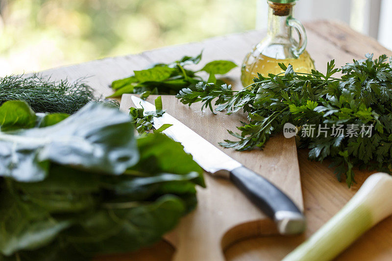 近距离拍摄的菜板，菜刀和各种香草和绿色蔬菜周围