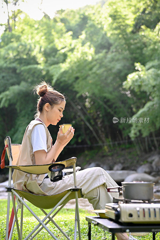 平静放松的年轻亚洲女性露营在营地，喝着早晨的咖啡。