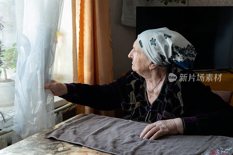 一位年长的妇女透过窗户看着街道。