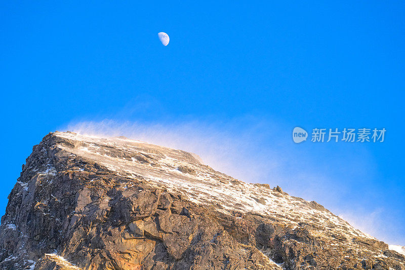 在挪威北部罗弗敦群岛，太阳，风和雪在山顶上的游戏，月亮在背景中看着它们。