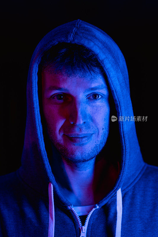 男性肖像在霓虹灯彩灯室内，男性穿着时尚卫衣。红色，蓝色，粉色和紫色。照片与未来主义的人，赛博朋克风格的概念。看镜头的人