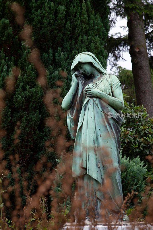 公园里站在树旁的老妇人的雕像
