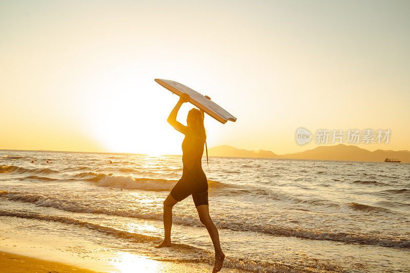 剪影的年轻女子在潜水服携带冲浪板以上的头