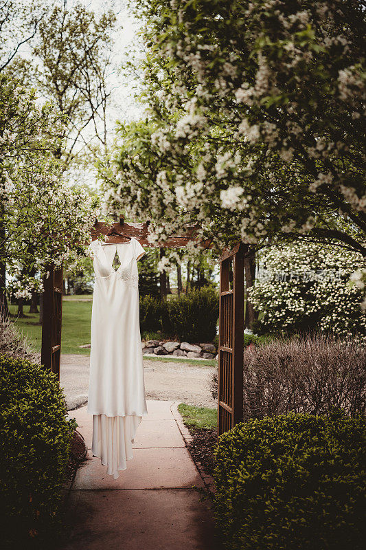 白色的婚纱挂在迎春花丛旁的凉亭上