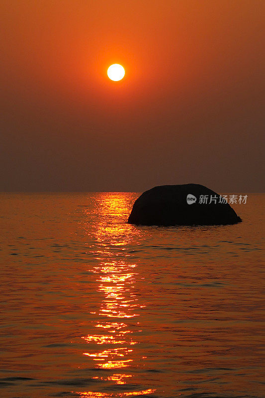 美丽的海边橙色日落日出映照在大海和潮湿的沙滩上，大海滩岩石在水中，潮汐反射涟漪，太阳落在海滩上