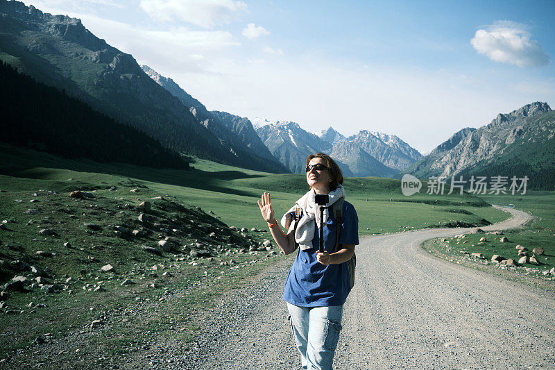 开朗的成熟女性背包客在天山的高地路上拍摄视频