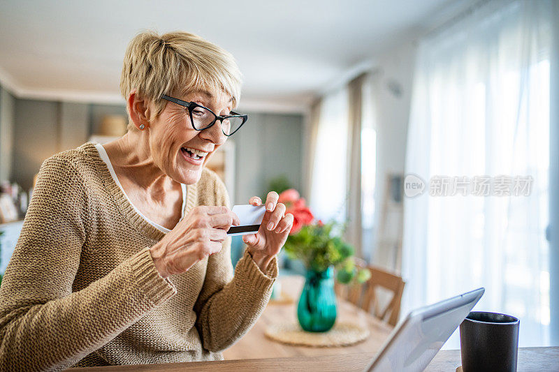 快乐的成熟女性在公寓里通过平板电脑进行网上银行业务