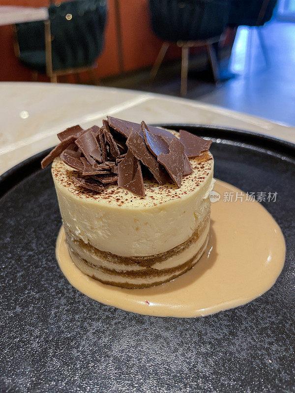 提拉米苏风格的个人芝士蛋糕餐厅甜点坐在奶油池，咖啡味布丁上面的巧克力刨花，奶油池，餐厅的桌子背景，重点在前景