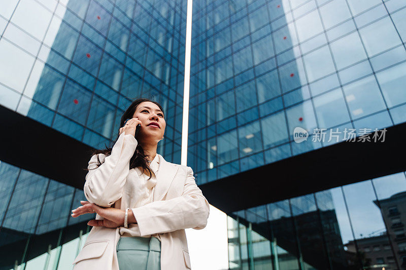 年轻优雅的亚洲职业商务女性在办公室外使用手机通话