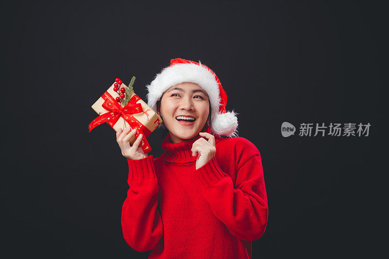 亚洲女人戴着圣诞老人的帽子开心地微笑着拿着许多礼盒，孤立在黑色的背景上。