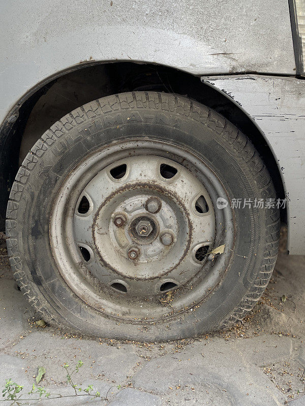 银色汽车轮拱上底漆划痕的特写图像，漏气的轮胎，停车事故，聚焦于前景