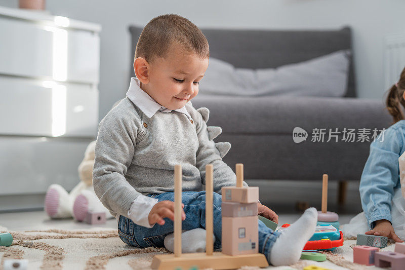 一个蹒跚学步的男孩在家里的地板上玩玩具