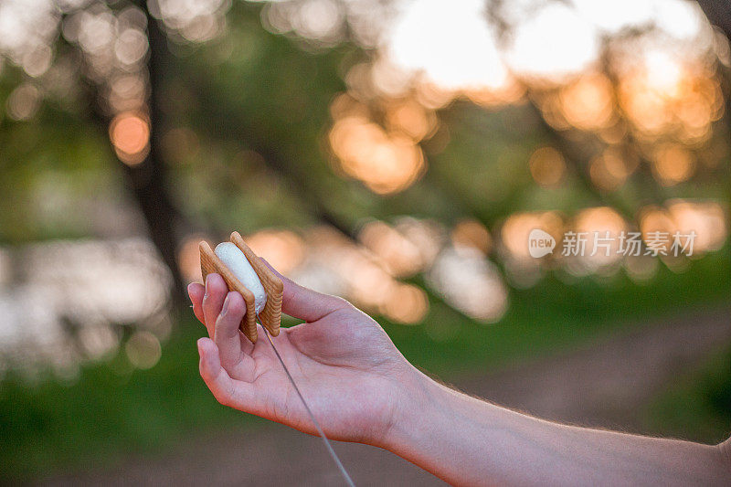 近距离的手拿着棉花糖和饼干做的S'more，在背景火