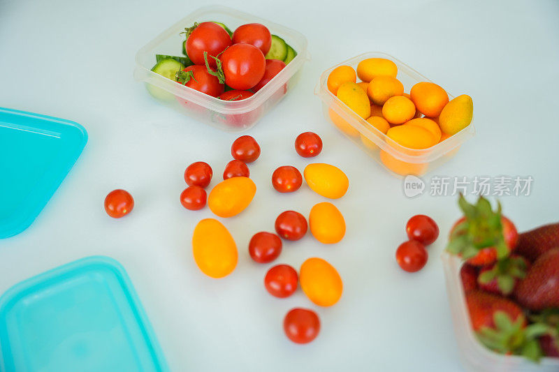 小西红柿、草莓和金橘装在透明的容器里，蓝色的背景