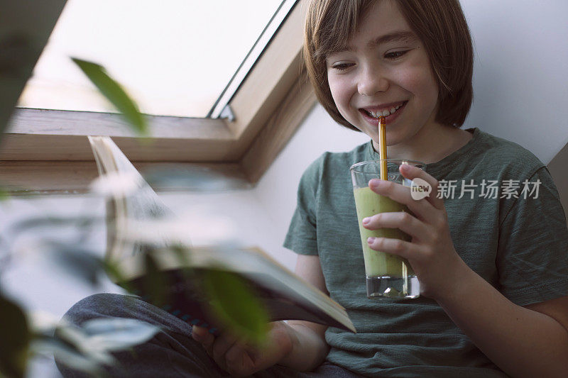 快乐的男孩在家里一边读书一边喝着健康的奶昔