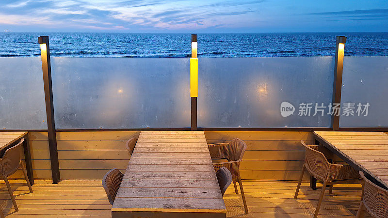 海边露台内部的碎片。有一张桌子和椅子，一个塑料挡风玻璃，还有带灯的柱子。天空和海浪都清晰可见。背景。