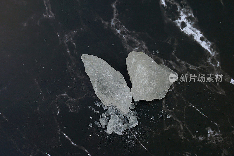 黑色背景上的明矾块。它是一种矿物，具有透明的白色晶体，无味，涩味，磨成类似冰糖的白色粉末。