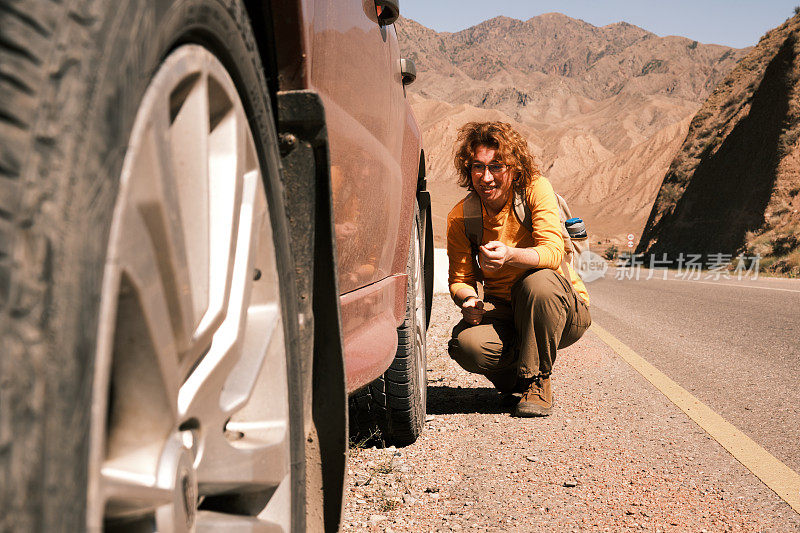 一名女游客在山路上的车出了问题，正在检查轮胎