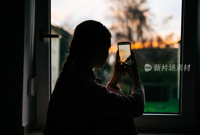 年轻的白人妇女在家里的窗户上拍摄日落。