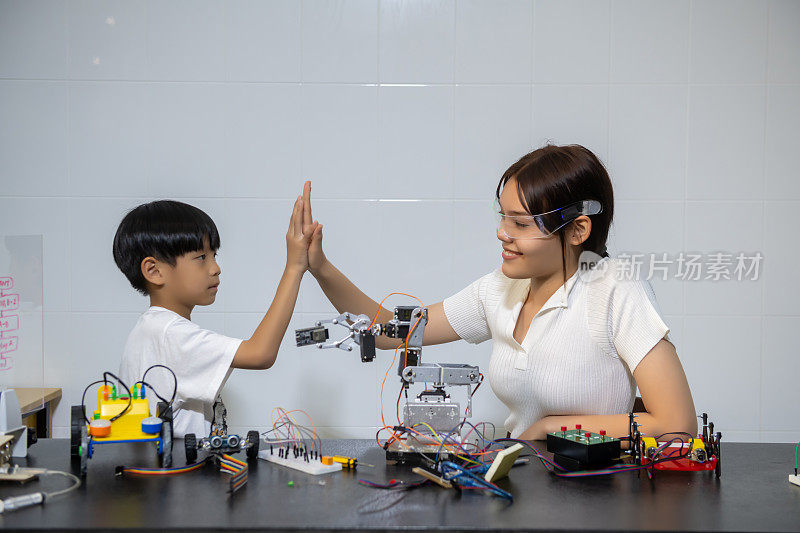 一群快乐的孩子在做机器人项目和击掌，集思广益专注于机器人的建造教育学习课程机器人学校科学技术爱好活动儿童家庭学校