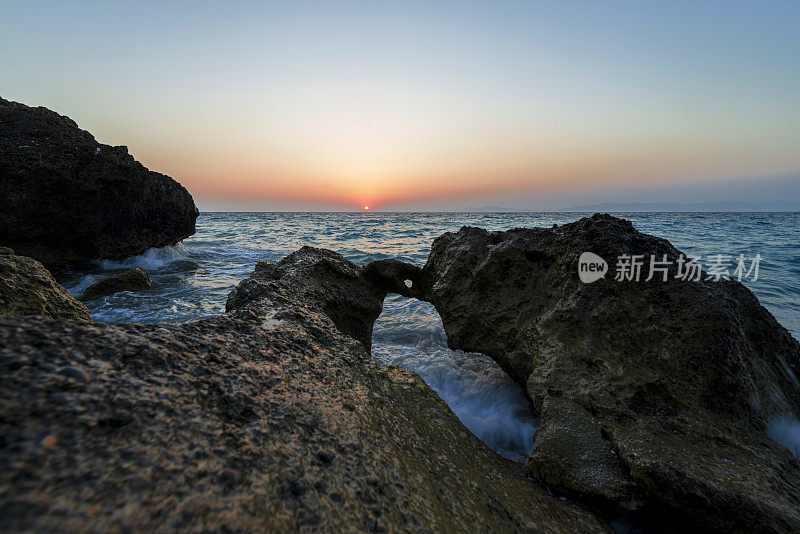 日落时海浪冲击着海岸线上的岩石。罗德岛，希腊