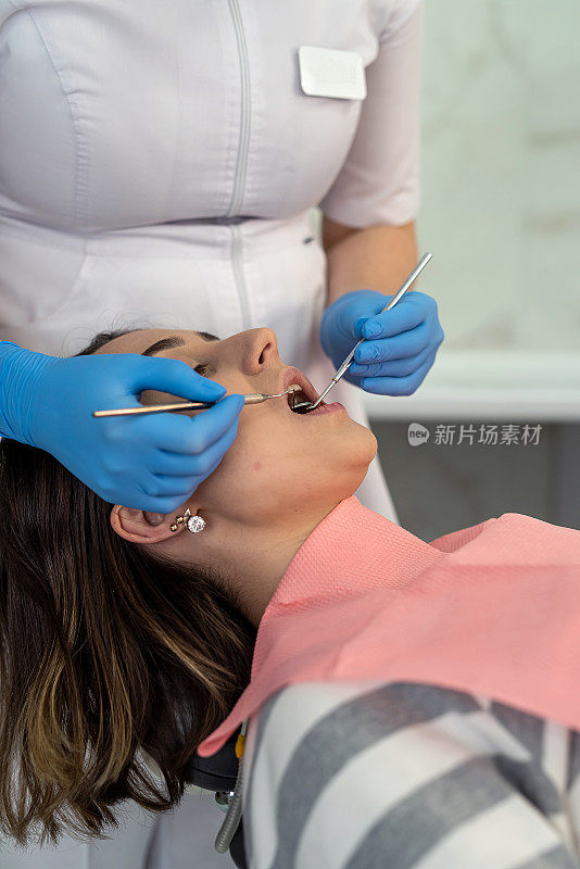 牙医使用牙科工具为她的女性客户进行口腔检查和检查蛀牙和牙龈
