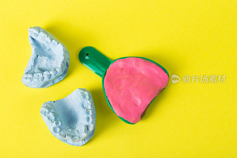 带海藻酸盐塑料块的牙科勺子，用于在黄色背景上拍摄牙颌的印象。黄色背景上的蓝色石膏牙颚。牙科正畸学，假牙和牙冠的制造。文本复制空间