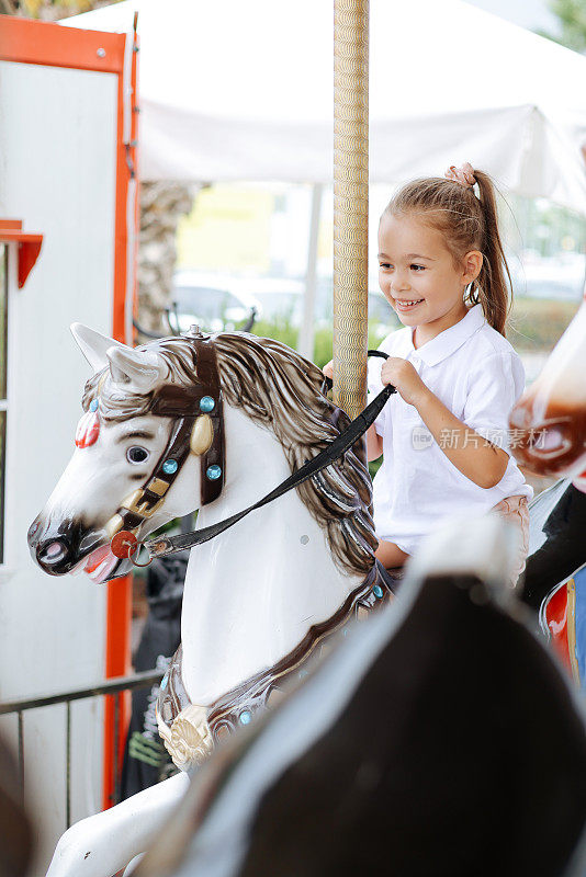 漂亮的孩子骑在旋转木马上。可爱的女孩是骑马的吸引力。有趣的庆祝活动