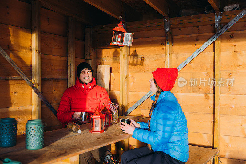 快乐的女人和男人在挪威的山上享受冬天的周末，在避难所喝茶