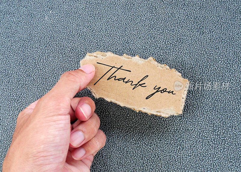 一名男子手持写有“谢谢”字样的破纸板卡片。