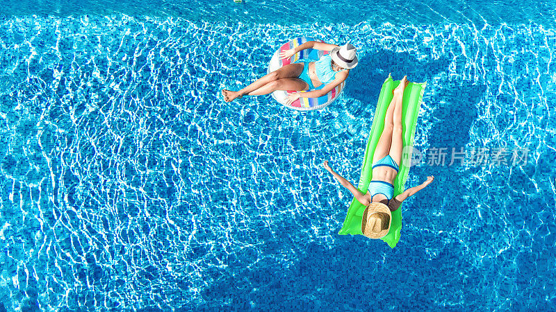 年轻的女孩在游泳池空中无人机从上面看，快乐的孩子们在充气环形甜甜圈和床垫上游泳，在度假胜地的家庭度假中在水里玩得很开心