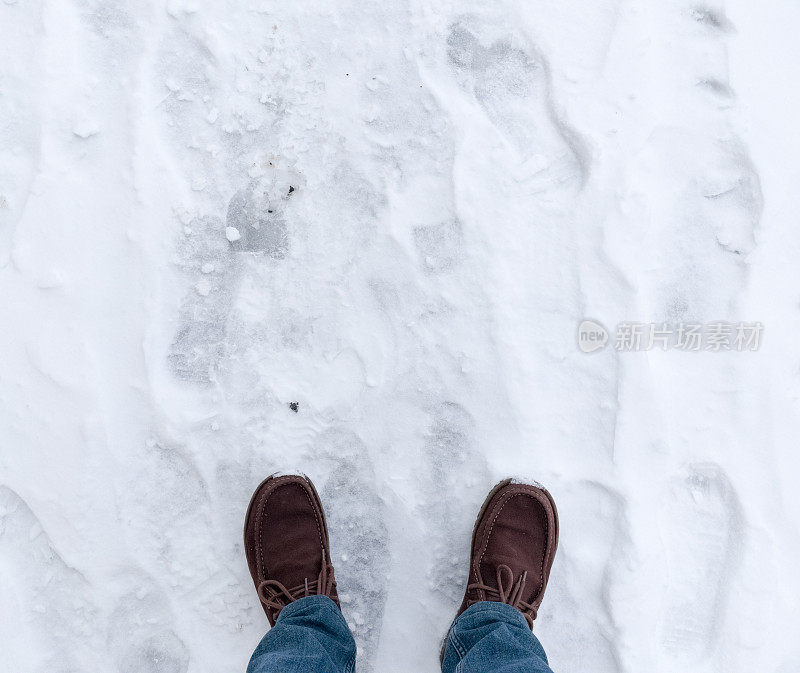 穿着靴子的脚踩在被雪覆盖的沥青上。