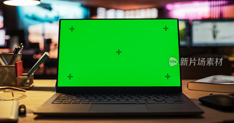 绿屏笔记本电脑，立在木桌上，高度可调。游戏开发启动的空装饰创意办公室的色度键显示