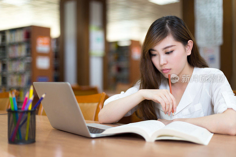 美丽的亚洲女学生使用笔记本电脑在图书馆学习