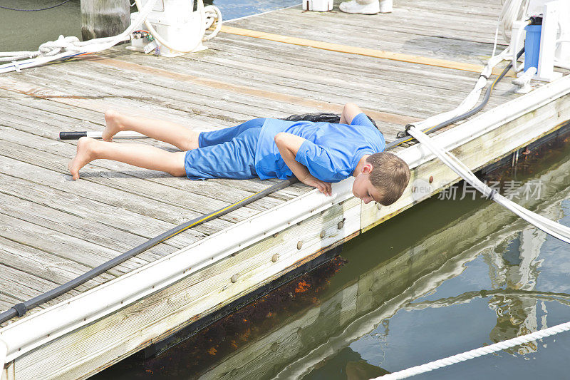一个白人男孩躺在码头上，用渔网向下看