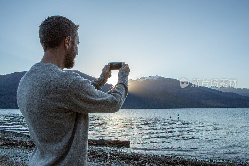 一名白人男子在湖边用智能手机拍照